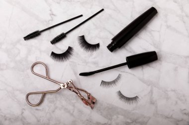 Takma kirpikli, rimel ve kirpik fırçalı, mermer arka planda kirpik bigudileri. Makyaj aletleri. Güzellik konsepti. Beste yap. Mesaj için yer. Kopyalanacak yer. Düz çizgi. MOCAP.