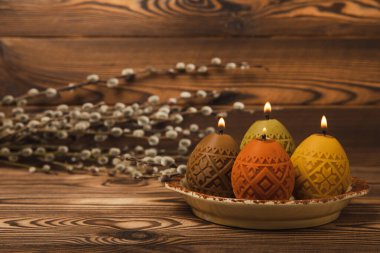 Kahverengi dokuma sehpasında söğüt filizli bir tabakta paskalya mumu yumurtaları. Paskalya tavşanı. Mutlu Paskalyalar. Paskalya mumları ve bahar çiçekleri..