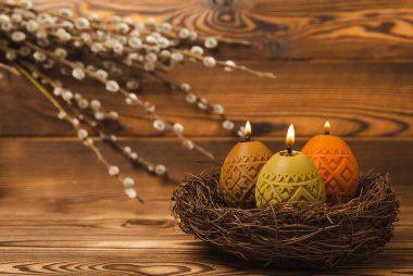 Kahverengi dokuma masasında söğüt dalları olan bir yuvadaki paskalya mumu yumurtaları. Paskalya tavşanı. Mutlu Paskalyalar. Paskalya mumları ve bahar çiçekleri..