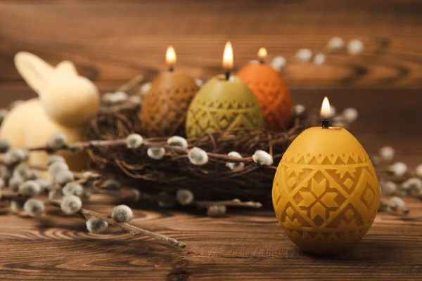 Easter candle eggs in a nest on a brown texture table with willow twigs. Easter bunny.Happy easter.Easter candles and spring flower.Spring holiday concept.Copy space.Close-up.