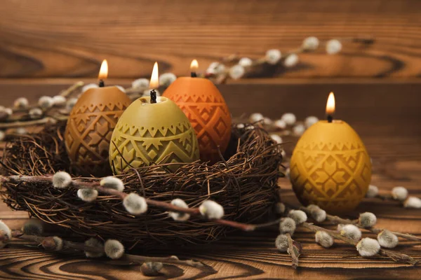 Easter candle eggs in a nest on a brown texture table with willow twigs. Easter bunny.Happy easter.Easter candles and spring flower.Spring holiday concept.Copy space.Close-up.