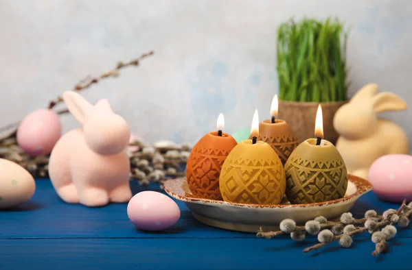 Easter candle eggs in a plate on a blue texture table with willow sprigs. Easter bunny.Happy easter.Easter candles and spring flower.Spring holiday concept.Copy space.Close-up.
