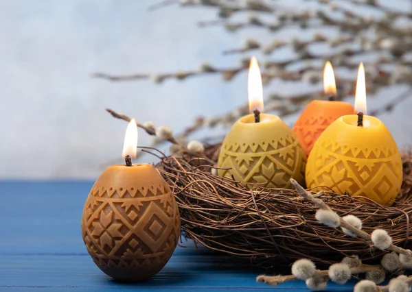 Easter candle eggs in a nest on a blue texture table with willow twigs. Easter bunny.Happy easter.Easter candles and spring flower.Spring holiday concept.Copy space.Close-up.