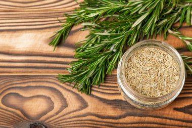 Taze biberiye ve kuru baharat tabakta ve kahverengi desenli arka planda kaşıklar. Taze baharat. Et ve balık çeşnisi. Tarif. Masada taze biberiye buketi. Mesaj için yer..