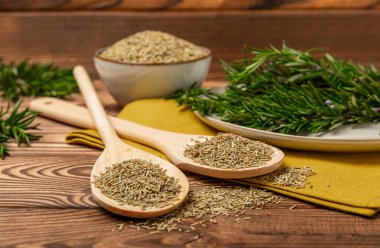 Taze biberiye ve kuru baharat tabakta ve kahverengi desenli arka planda kaşıklar. Taze baharat. Et ve balık çeşnisi. Tarif. Masada taze biberiye buketi. Mesaj için yer..