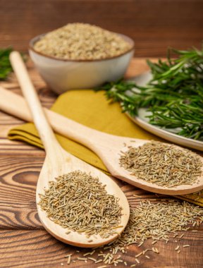 Taze biberiye ve kuru baharat tabakta ve kahverengi desenli arka planda kaşıklar. Taze baharat. Et ve balık çeşnisi. Tarif. Masada taze biberiye buketi. Mesaj için yer..