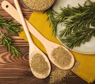 Taze biberiye ve kuru baharat tabakta ve kahverengi desenli arka planda kaşıklar. Taze baharat. Et ve balık çeşnisi. Tarif. Masada taze biberiye buketi. Mesaj için yer..