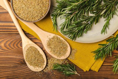 Taze biberiye ve kuru baharat tabakta ve kahverengi desenli arka planda kaşıklar. Taze baharat. Et ve balık çeşnisi. Tarif. Masada taze biberiye buketi. Mesaj için yer..