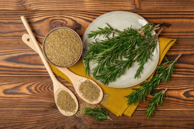 Taze biberiye ve kuru baharat tabakta ve kahverengi desenli arka planda kaşıklar. Taze baharat. Et ve balık çeşnisi. Tarif. Masada taze biberiye buketi. Mesaj için yer..