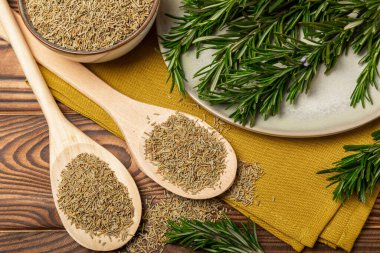 Taze biberiye ve kuru baharat tabakta ve kahverengi desenli arka planda kaşıklar. Taze baharat. Et ve balık çeşnisi. Tarif. Masada taze biberiye buketi. Mesaj için yer..