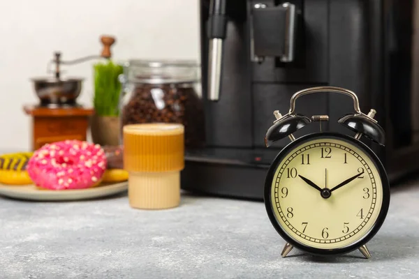 Alarm clock and a cup of morning coffee with a coffee machine on the background of the kitchen interior.A glass of coffee on the table with a clock in the morning. Good morning concept. WAKE UP! Morning time concept
