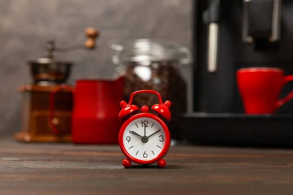 Alarm clock and a cup of morning coffee with a coffee machine on the background of the kitchen interior.A glass of coffee on the table with a clock in the morning. Good morning concept. WAKE UP! Morning time concept