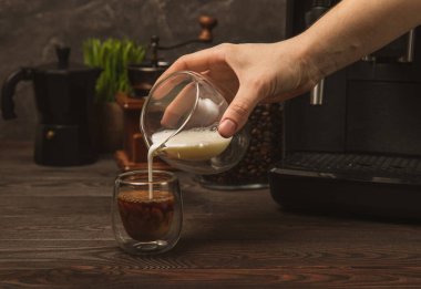 Kahvenin içine krema döküyorum. Kahve içiyorum. Siyah masa arkasına. Sabah kahvesi. Neşeli sabah konsepti. Kahveye süt dökmenin kavramsal bileşimi. Enerji içeceği. Metin için yer.