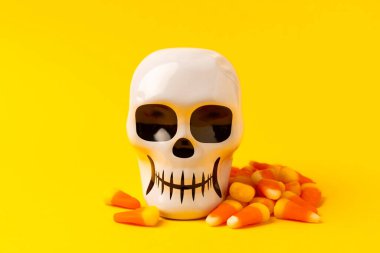 Cadılar Bayramı 'nda mısır şekeri ve şeker kafatası sarı arka planda. Cadılar Bayramı için klasik şeker şekeri. Cadılar bayramı konsepti, mısır şekeri ve balkabağı feneri..