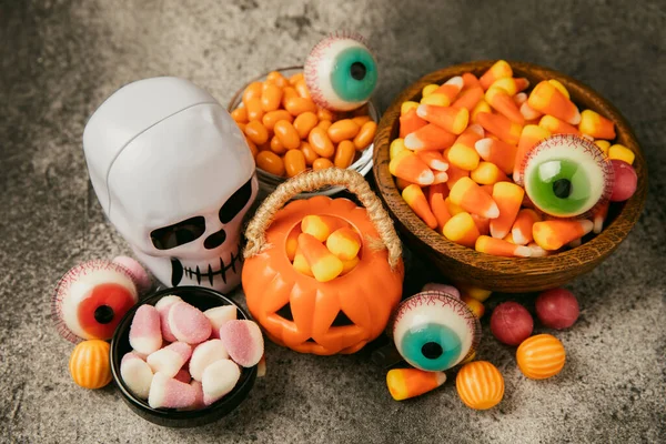 Halloween candy corn,jelly eye, pumpkin candy, sugar skull in different bowls on black background.Classic candy sweets for Halloween with.Halloween holiday concept with candy corn and jack o lantern.