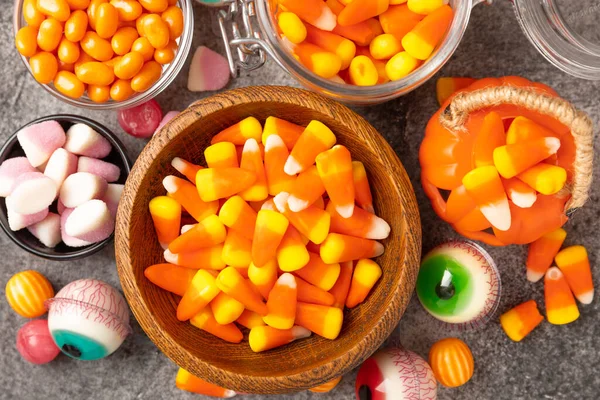 Halloween candy corn,jelly eye, pumpkin candy, sugar skull in different bowls on black background.Classic candy sweets for Halloween with.Halloween holiday concept with candy corn and jack o lantern.