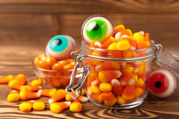 Halloween candy corn and jelly eye in glass jar on brown background.Classic white,orange and yellow candy sweets for Halloween with.Halloween holiday concept with candy corn and Jack-o-lantern.