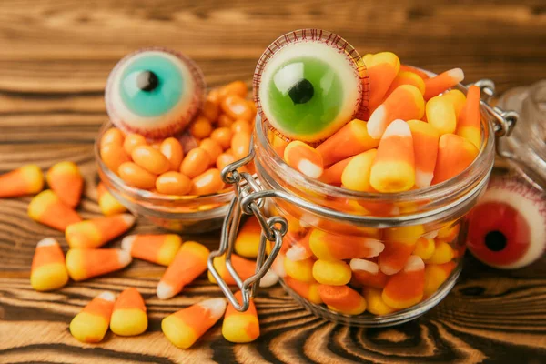 Halloween candy corn and jelly eye in glass jar on brown background.Classic white,orange and yellow candy sweets for Halloween with.Halloween holiday concept with candy corn and Jack-o-lantern.