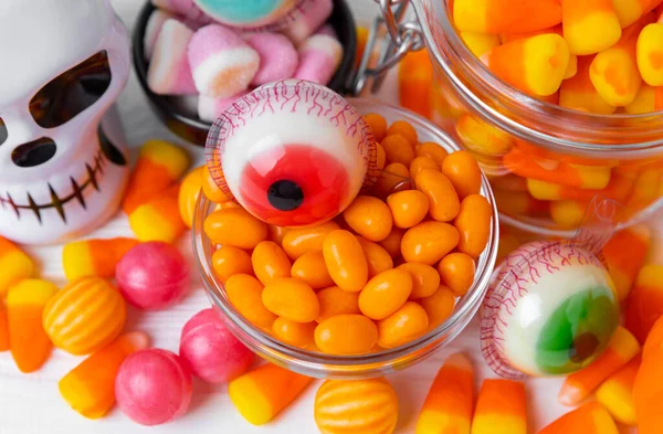 Halloween candy corn,jelly eye, pumpkin candy, sugar skull in different bowls on white background.Classic candy sweets for Halloween with.Halloween holiday concept with candy corn and jack o lantern.