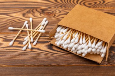 Kahverengi desenli bir ahşabın üzerindeki el işi kutusunda pamuk çubukları. Bambu pamuk tomurcukları. Kulakların hijyeni için. Çevre dostu materyaller. Hijyenik pamuk tokaları..