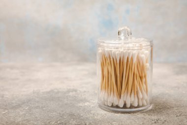 El işi ambalajında pamuk çubukları ve gri çimento arka planında tutucu. Bambu pamuk tomurcukları. Kulakların hijyeni için. Çevre dostu materyaller. Hijyenik pamuk tokaları..