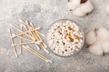 El işi ambalajında pamuk çubukları ve gri çimento arka planında tutucu. Bambu pamuk tomurcukları. Kulakların hijyeni için. Çevre dostu materyaller. Hijyenik pamuk tokaları..