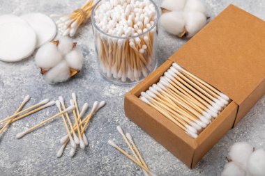 El işi ambalajında pamuk çubukları ve gri çimento arka planında tutucu. Bambu pamuk tomurcukları. Kulakların hijyeni için. Çevre dostu materyaller. Hijyenik pamuk tokaları..