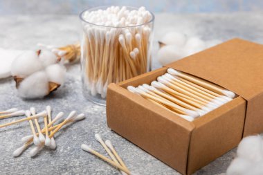 El işi ambalajında pamuk çubukları ve gri çimento arka planında tutucu. Bambu pamuk tomurcukları. Kulakların hijyeni için. Çevre dostu materyaller. Hijyenik pamuk tokaları..