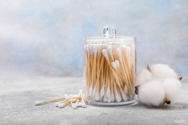 El işi ambalajında pamuk çubukları ve gri çimento arka planında tutucu. Bambu pamuk tomurcukları. Kulakların hijyeni için. Çevre dostu materyaller. Hijyenik pamuk tokaları..