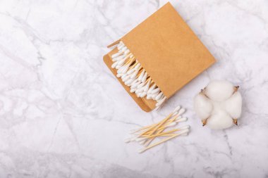 Beyaz mermer arka planda el işi ambalajında pamuk çubukları. Bambu pamuk tomurcukları. Kulakların hijyeni için. Çevre dostu materyaller. Hijyenik pamuk tokaları..