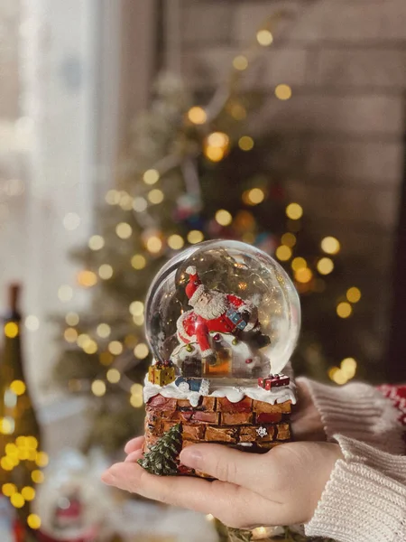 クリスマスツリーを背景に鹿とクリスマスの装飾が施されたサンタクロースの人形で魔法の雪の地球 女性の手で雪の地球 新年とクリスマスの概念 おとぎ話 — ストック写真