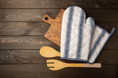 Ahşap mutfak aletleri, kesim tahtası, tutacağı ve eldiven masanın üstünde. Mutfak eldiveni ve koruyucu fırın eldivenleri masanın üstünde. Mutfak eşyaları. Mutfak aksesuarları. Yakın çekim. Üst manzara..