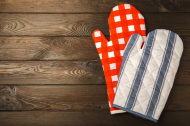 Tutucu ve Mutfak Mitten kahverengi ahşap arka planda. Masanın üstünde koruyucu fırın eldivenleri. Mutfak eşyaları. Mutfak aksesuarları. Yakın plan. Metin için yeri olan üst görünüm.