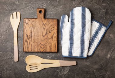 Ahşap mutfak aletleri, kesim tahtası, tutacağı ve eldiven masanın üstünde. Mutfak eldiveni ve koruyucu fırın eldivenleri masanın üstünde. Mutfak eşyaları. Mutfak aksesuarları. Yakın çekim. Üst manzara..