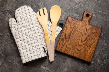Ahşap mutfak aletleri, kesim tahtası, tutacağı ve eldiven masanın üstünde. Mutfak eldiveni ve koruyucu fırın eldivenleri masanın üstünde. Mutfak eşyaları. Mutfak aksesuarları. Yakın çekim. Üst manzara..