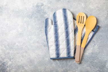 Ahşap mutfak aletleri, tutacağı ve eldivenler masanın üstünde, üst manzara. Mutfak eldiveni, fırın eldiveni ve gri mermer masada ahşap çatal bıçak takımı. Mutfak aksesuarları. Mutfak konsepti..