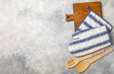 Ahşap mutfak aletleri, kesim tahtası, tutacağı ve eldiven masanın üstünde. Mutfak eldiveni ve koruyucu fırın eldivenleri masanın üstünde. Mutfak eşyaları. Mutfak aksesuarları. Yakın plan. Metin için yeri olan üst görünüm.