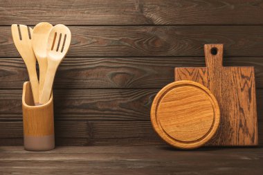 Kahverengi duvardaki tahta ve mutfak gereçleri kesme tahtası ve mutfak gereçleri. Mutfak gereçleri ahşap masa üstünde duruyor, yazı için boş alan, ön görüş. Tarif. MOCKUP.Yemek kavramı..