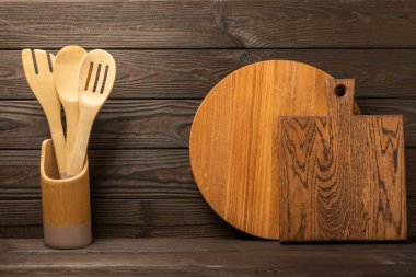 Kahverengi duvardaki tahta ve mutfak gereçleri kesme tahtası ve mutfak gereçleri. Mutfak gereçleri ahşap masa üstünde duruyor, yazı için boş alan, ön görüş. Tarif. MOCKUP.Yemek kavramı..