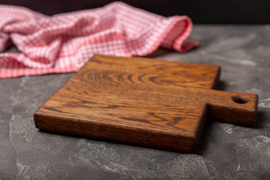 Ahşap mutfak masasında havlunun üzerinde tahta kesme tahtası. Siyah desenli arka planda kesme tahtası ve mutfak havlusu. Menü yemek kartı ya da yemek tarifleri arka plan kavramı. MOCKUP Tasarım. Metin için yer, kopyalama alanı.