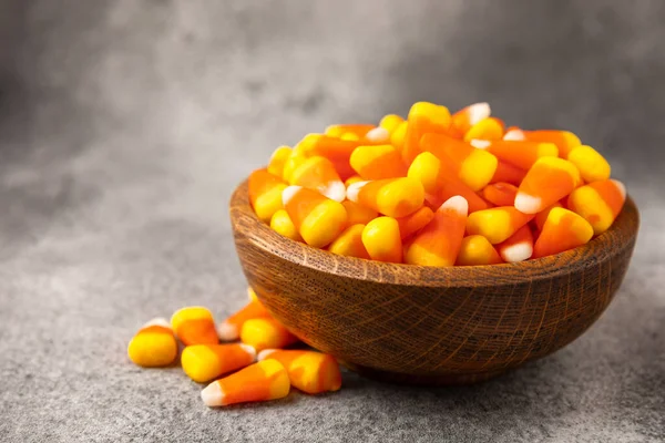 Candy corn. Classic white, orange and yellow Halloween lollipops. Sweet pumpkin gummies in a wooden bowl on a black marble background.Copy space.Place for text. Holiday concept.