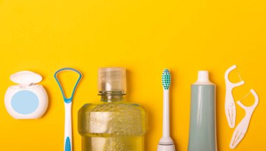 Sonik elektrikli diş fırçası, diş macunu, gargara, diş ipi ve dil temizleyicisi sarı arka planda. Ağız temizliği. Diş bakımı. Diş hekimliği konsepti. Metnin yeri..