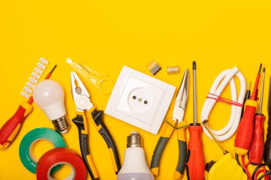 Sarı zemin üzerindeki elektrik teçhizatı kopya alanı ile üst görünüm. Elektrik aracı seti. Çoklu metre, testçi, tornavida, kesiciler, koli bandı, lamba, mezura, mezura ve kablo..