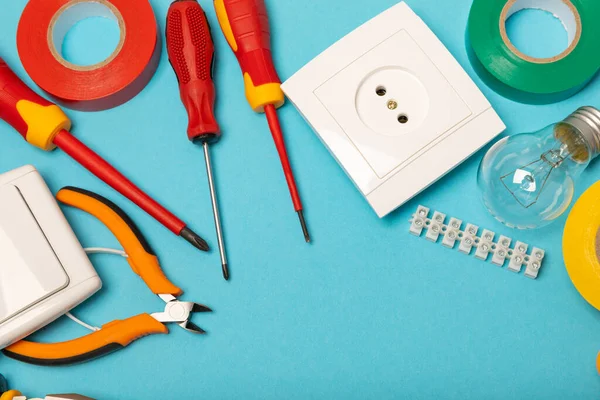 Mavi arka planda kopyalanmış elektrik teçhizatı. Üst görünüm. Elektrik aracı seti. Çoklu metre, test cihazı, tornavida, kesici, koli bandı, lamba, mezura, mezura ve kablo..