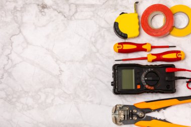 Beyaz mermer arka planda elektrikli aletler. Multimetre, inşaat bandı, elektrik bandı, tornavida, pense, otomatik yalıtım striptizcisi, soket ve LED lambası. Düz konsept. Elektrik kutusu..
