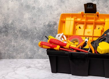 Beyaz mermer arka planda elektrikli aletler. Multimetre, inşaat bandı, elektrik bandı, tornavida, pense, otomatik yalıtım striptizcisi, soket ve LED lambası. Düz konsept. Elektrik kutusu..