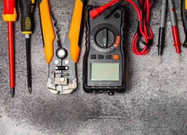 Siyah mermer arka planda elektrikli aletler. Multimetre, inşaat bandı, elektrik bandı, tornavida, pense, otomatik yalıtım striptizcisi, soket ve LED lamba. Düz konsept..