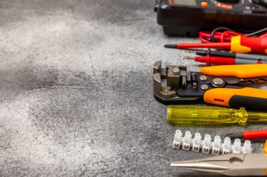 Siyah mermer arka planda elektrikli aletler. Multimetre, inşaat bandı, elektrik bandı, tornavida, pense, otomatik yalıtım striptizcisi, soket ve LED lamba. Düz konsept..