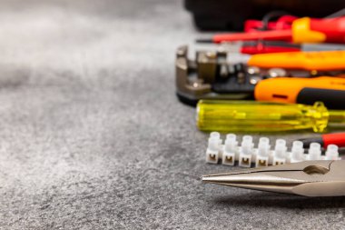 Siyah mermer arka planda elektrikli aletler. Multimetre, inşaat bandı, elektrik bandı, tornavida, pense, otomatik yalıtım striptizcisi, soket ve LED lamba. Düz konsept..