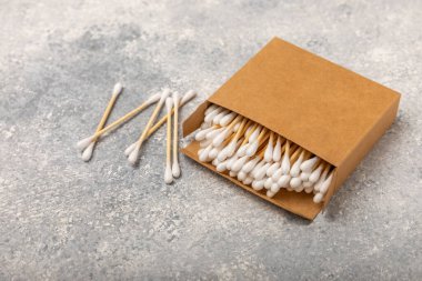 Dokulu bir arka planda eko kraft ambalajında pamuk tomurcukları. Beyaz arka planda pamuklu çubuk. Burun ve kulaklarda hijyen çubukları. Bambu pamuk tomurcukları. Eko-dost. Mesaj için yer. Kopya için yer..